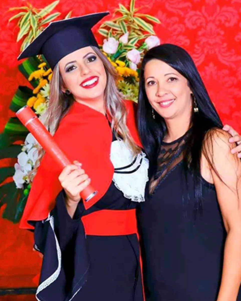 Flavinha com beca e diploma durante sua formatura em Direito, ao lado de uma familiar